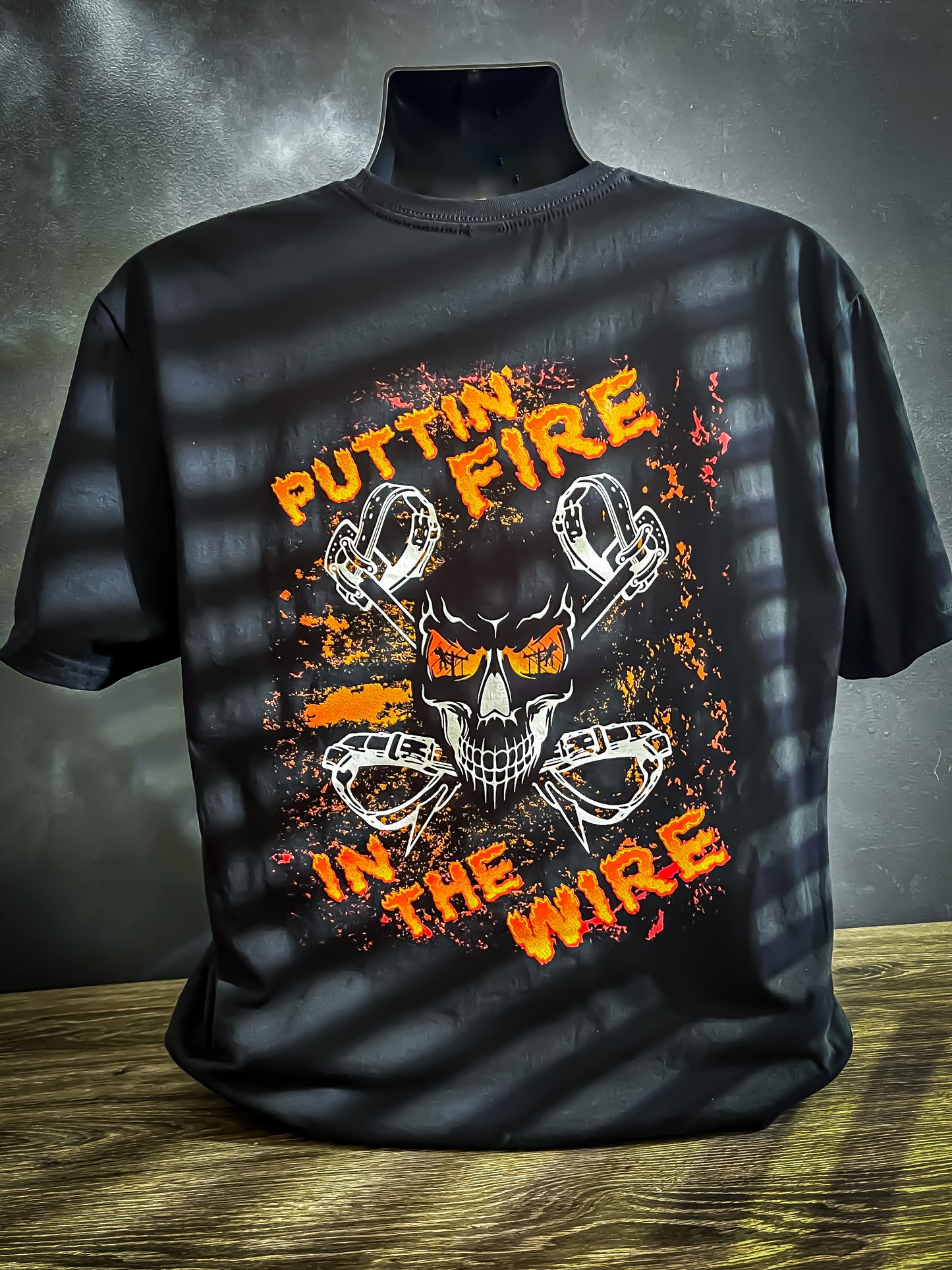 Black t-shirt with fiery skull graphic and the words "Puttin' Fire in the Wire" in bold orange text, surrounded by lineman tools.