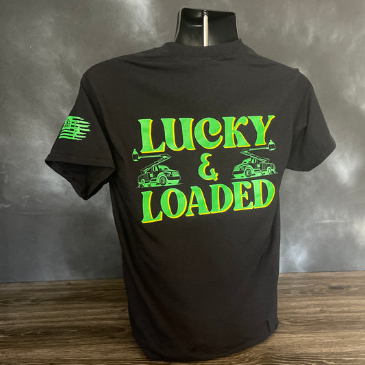 A black T-shirt featuring the bold text "Lucky & Loaded" in green and yellow, with two bucket trucks on either side of the text. The sleeve has the LineCrate logo and flag graphic. Designed for LineMen, this shirt showcases pride in the line trade with a modern fit and durable cotton fabric.