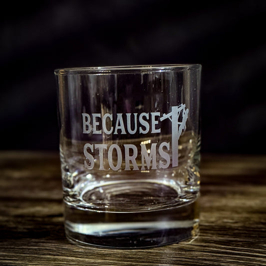 Clear whiskey glass with the phrase "Because Storms" etched on the front, featuring a lineman silhouette on a power pole, symbolizing the hard work and dedication of LineMen during storm recovery efforts.