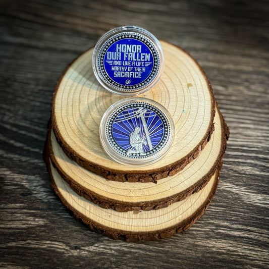 Honor Our Fallen challenge coin featuring blue and silver design, with tribute message on one side and lineman kneeling beneath power lines on the other, in a clear protective case