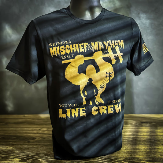 Black t-shirt with yellow lettering that says, "Whenever Mischief & Mayhem Ensue, You Will Find Line Crew," featuring a silhouette of a LineMan and utility poles in the background. The sleeve displays the LineCrate flag logo with a LineMan on a pole.